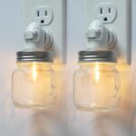 Two clear glass Mason jar night lights with brushed plastic bases, plugged into wall outlets, emitting a warm glow.