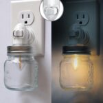 Two clear glass Mason jar night lights with brushed plastic bases, plugged into wall outlets, emitting a warm glow.