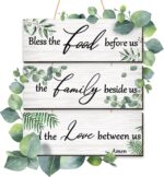 Three Maitys eucalyptus greenery wooden wall signs with 'Bless Family Food Love' text, hung on a rustic wall.